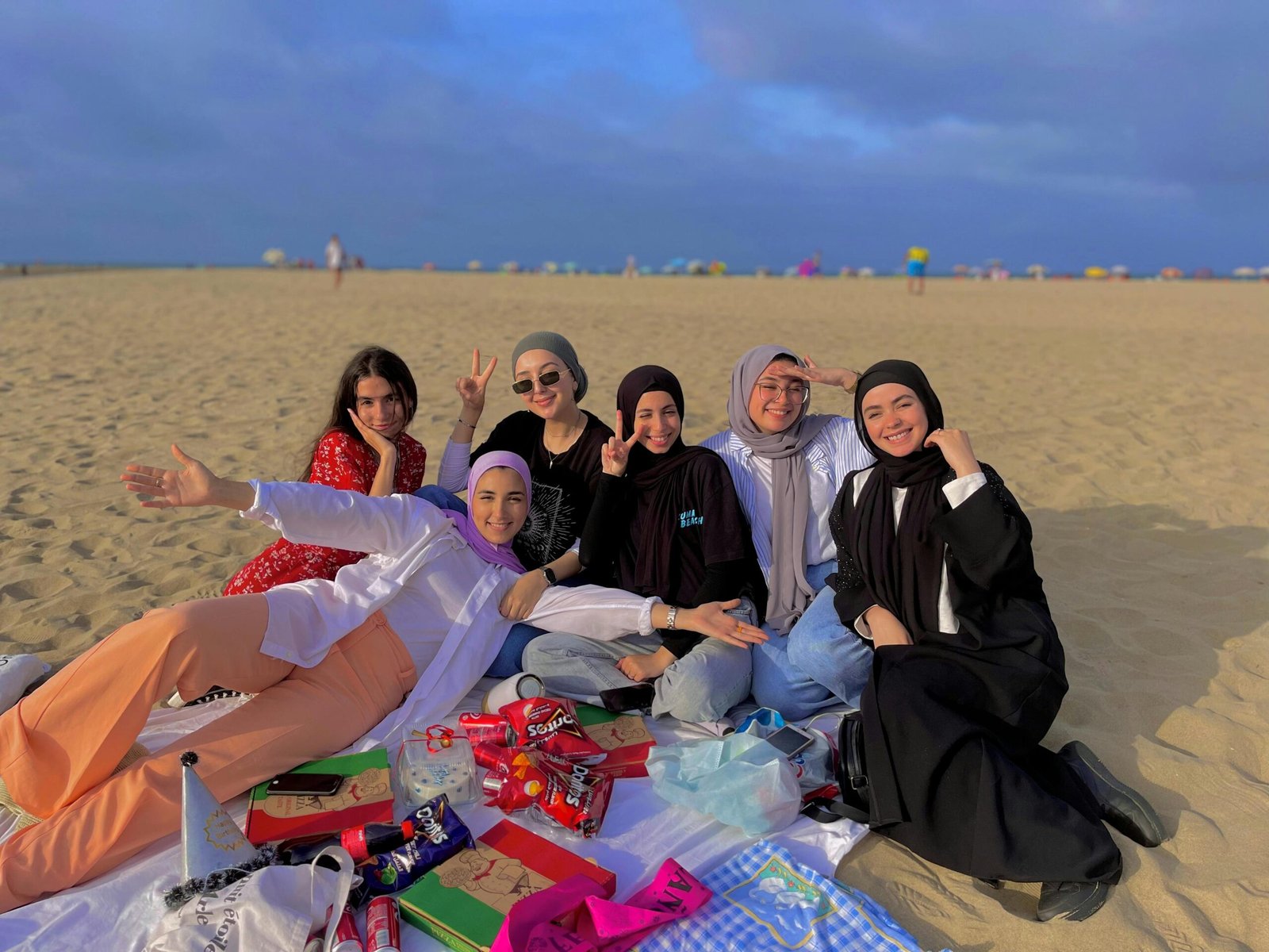 ELOA STORE Group of women having a relaxed picnic on the sandy beach of Martil in Morocco, wearing traditional and casual attire.